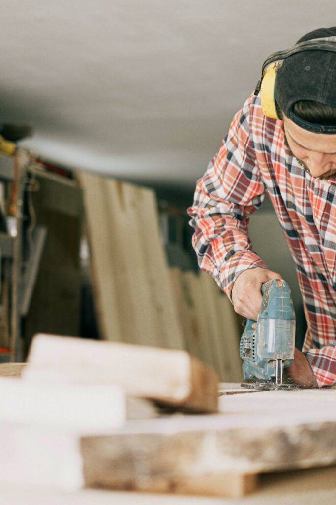 A skilled carpenter uses a power drill in a well-organized woodworking workshop.